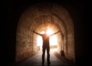 joyous man standing victorious at end of tunnel with light shining to guide the way out